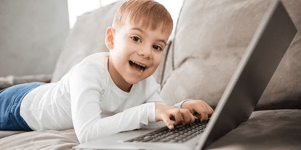 A smiling boy using a laptop while lying down in his stomach.