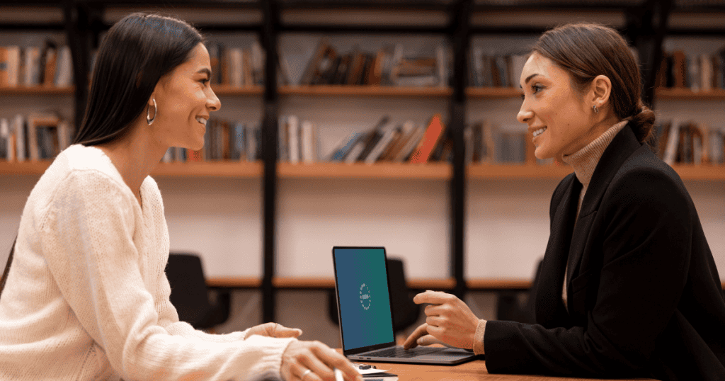 Two professionals engage in an earnest face-to-face conversation over a laptop, highlighting the personal responsibility and potential liability involved in professional consulting.
