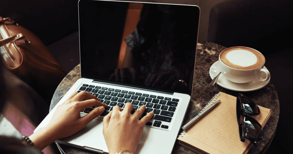 A person's hands are typing on a silver laptop next to a cup of coffee and a notebook; the five-step process of selecting a profitable focus starts right here.