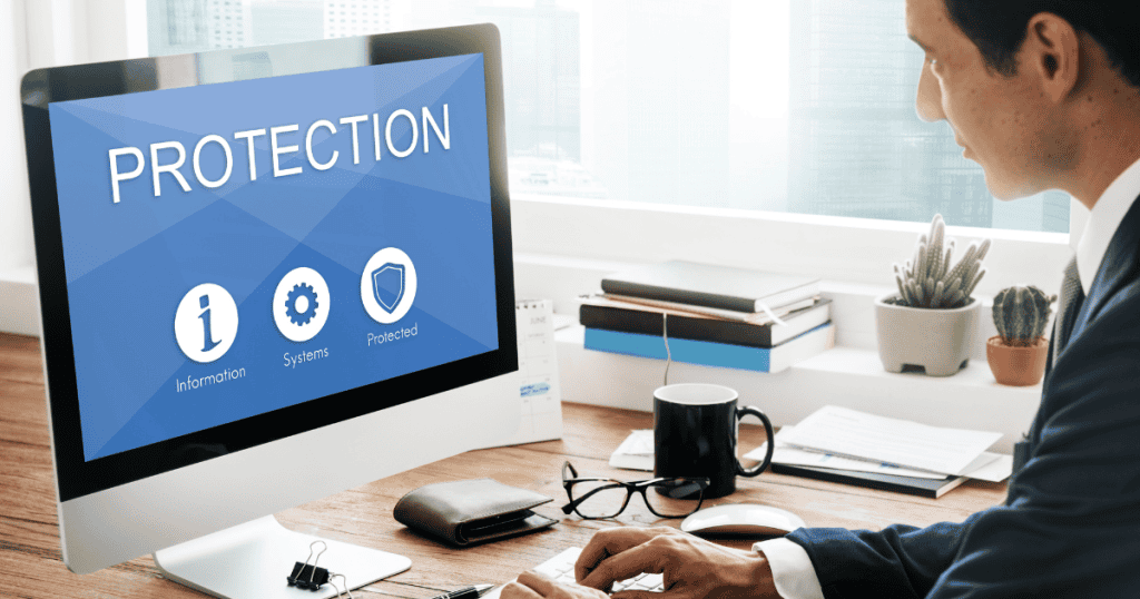 A man works at a desk facing a large monitor with "Protection" status icons, representing the foundational security measures established at the very beginning of a project.