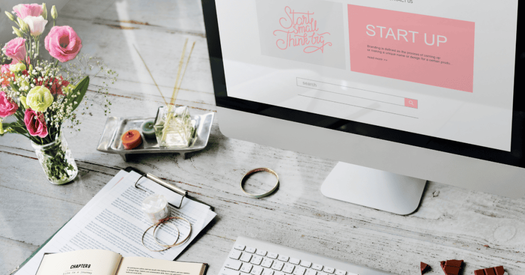 A minimalist workspace features a computer screen alongside fresh flowers and stationery, highlighting a creative layout for launching new digital ventures.