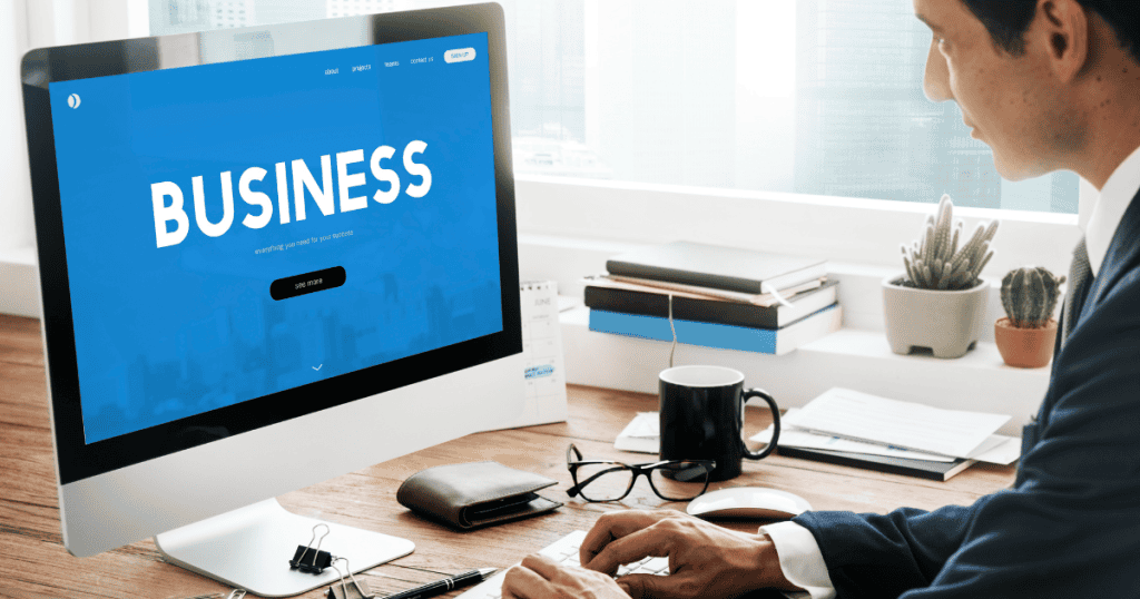 A professional man works at a desk in front of a large monitor, which displays a sleek blue landing page designed for corporate growth.