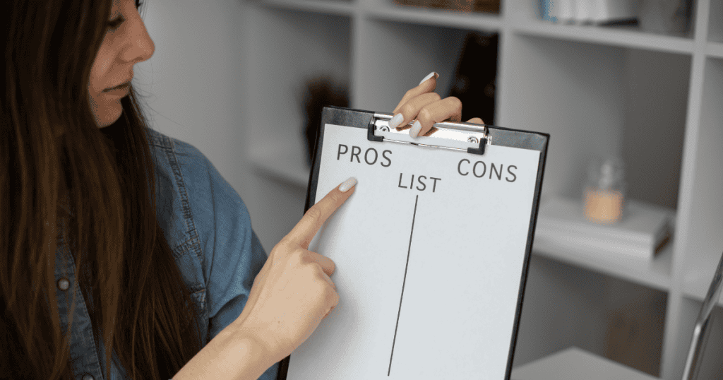 A woman points to the 'pros' column on a clipboard comparison sheet, demonstrating the analytical steps needed to finalize a single direction from many options.