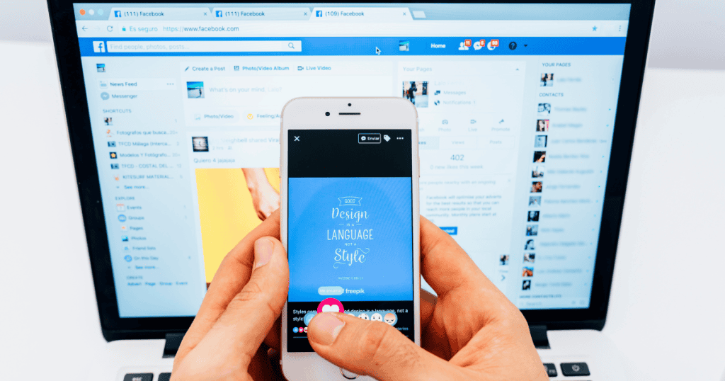 A person holds a smartphone displaying a graphic design post in front of a laptop running Facebook, mirroring the repetitive nature of cross-platform distribution.