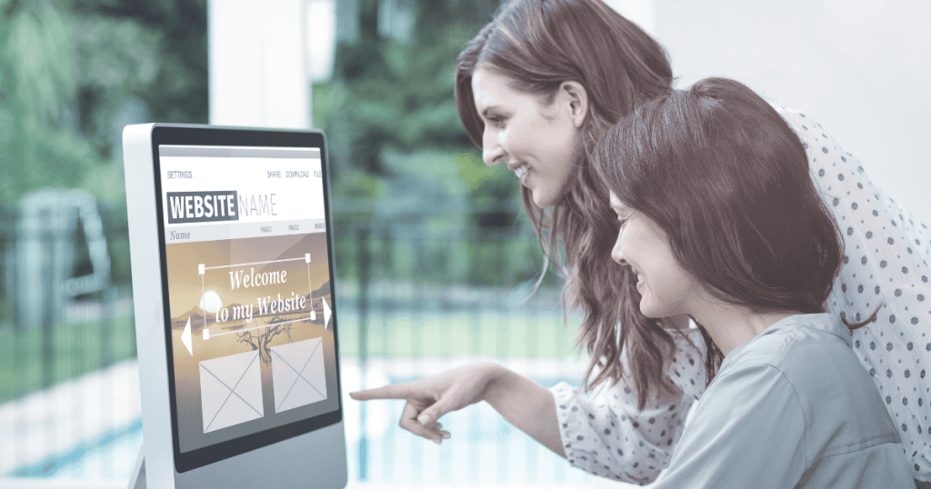 Two women smiling while looking at a website template on a monitor, capturing a moment of early-stage creative inspiration and collaborative growth.