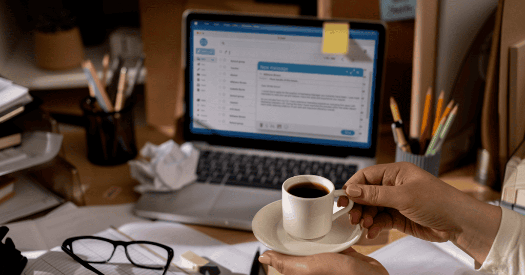 A person holding a cup of coffee at a desk with an open email client on a laptop, highlighting the importance of direct connection in a digital workspace.