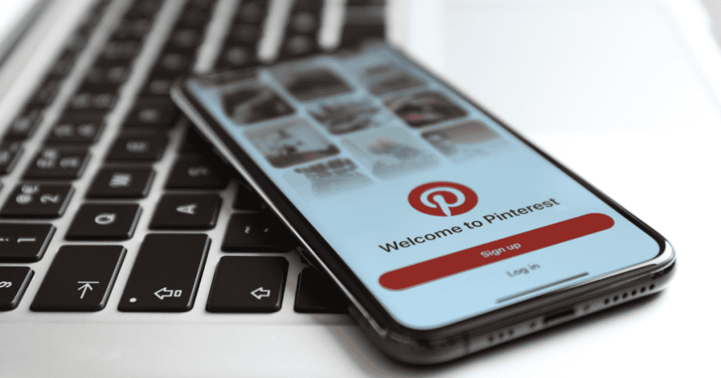 A smartphone resting on a laptop keyboard shows a visual discovery app's welcome screen, highlighting the mobile-first approach to curated content inspiration.