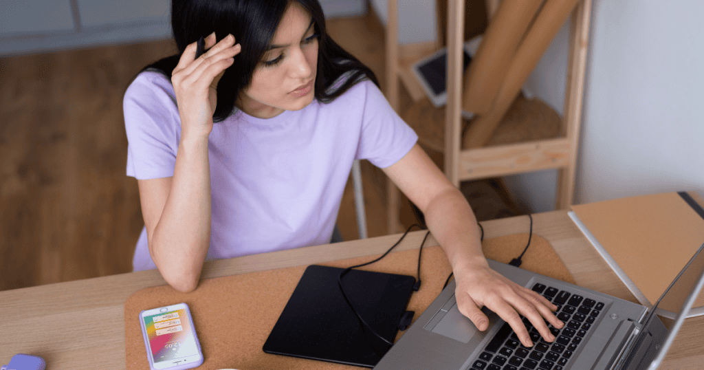A woman resting her head on her hand while working at a laptop with a graphic tablet, illustrating the thoughtful process of refining and adjusting a creative project.