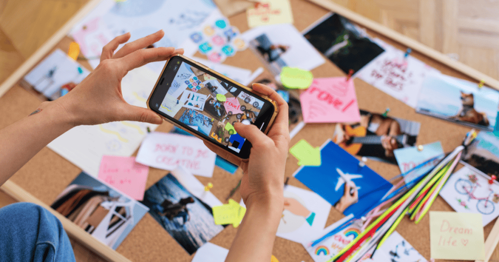 A person uses a smartphone to photograph a curated mood board, showcasing the deliberate selection of creative elements for public sharing.