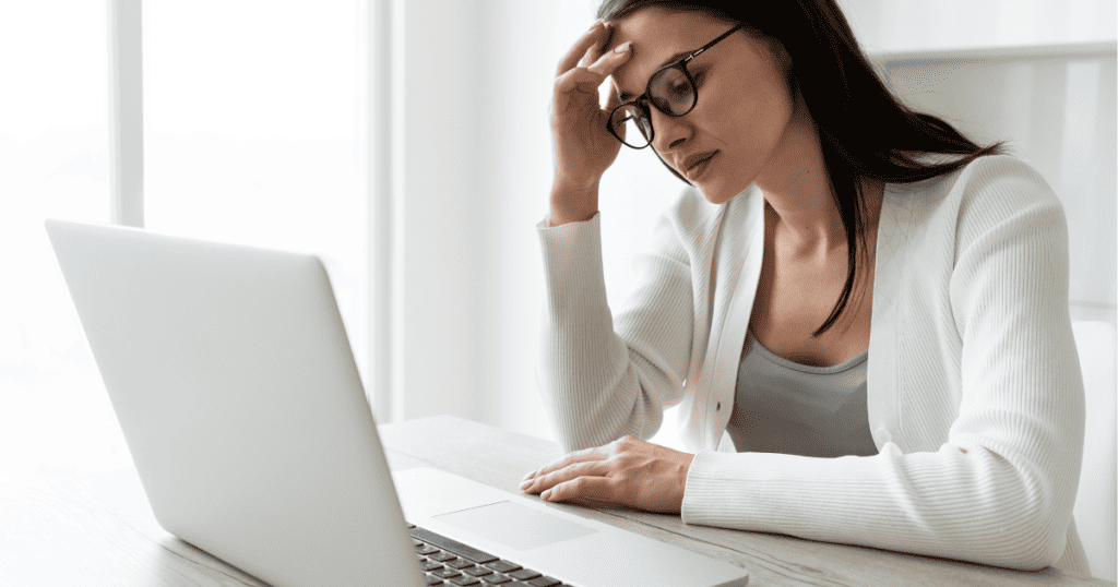 A woman at a desk leaning her head on her hand with an exhausted expression, capturing the heavy toll of an unsustainable pace.
