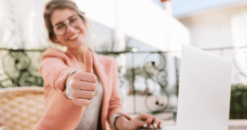 A woman gives a cheerful thumbs-up behind an open laptop, capturing the confidence that comes with following a structured plan for success.
