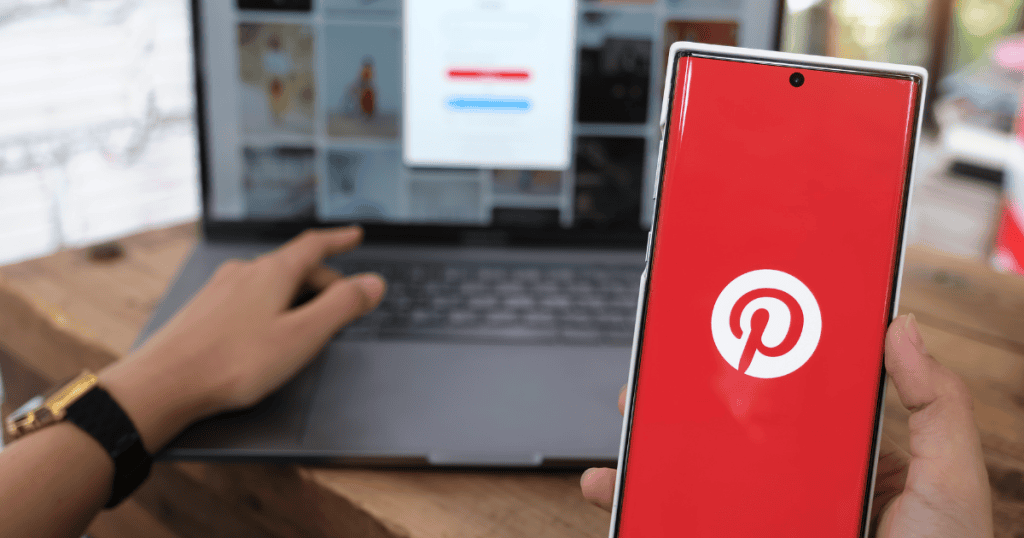 A person holding a smartphone displaying the Pinterest logo while working on a laptop, capturing the transition from social engagement to sustainable results.