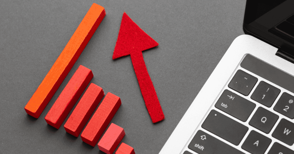 A red arrow pointing upward next to a rising bar graph and a laptop keyboard, illustrating a strategic upward trend in digital performance.