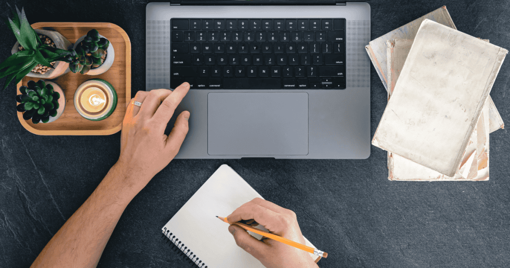 An overhead view captures a person typing on a laptop while keeping a physical notebook ready, highlighting a focus on direct and accessible communication.