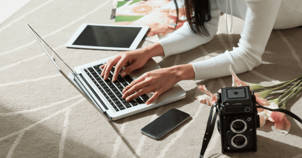 A person works on a laptop on the floor surrounded by a camera and scattered photos, capturing the essence of grounding ideas in real-world details.